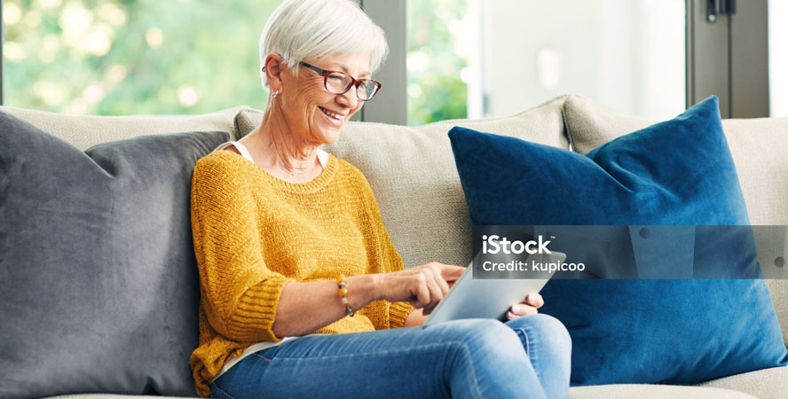 For Individuals - Female senior sitting on a couch using a tablet to review her medication list.