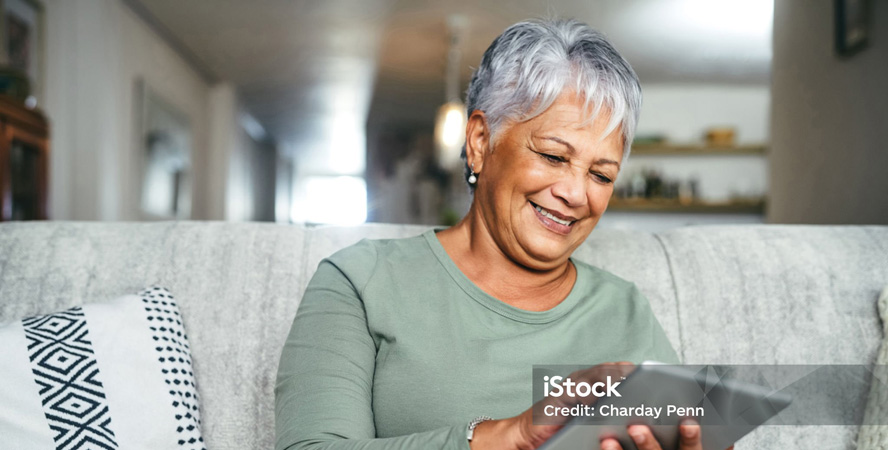 Female senior sitting on a couch using a tablet to review her medication list.